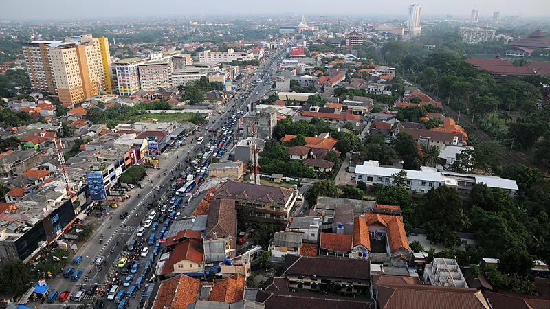 Pemandangan udara Kota Depok dengan jalan utama padat kendaraan membelah permukiman beratap merah, ruko, dan gedung bertingkat di kejauhan