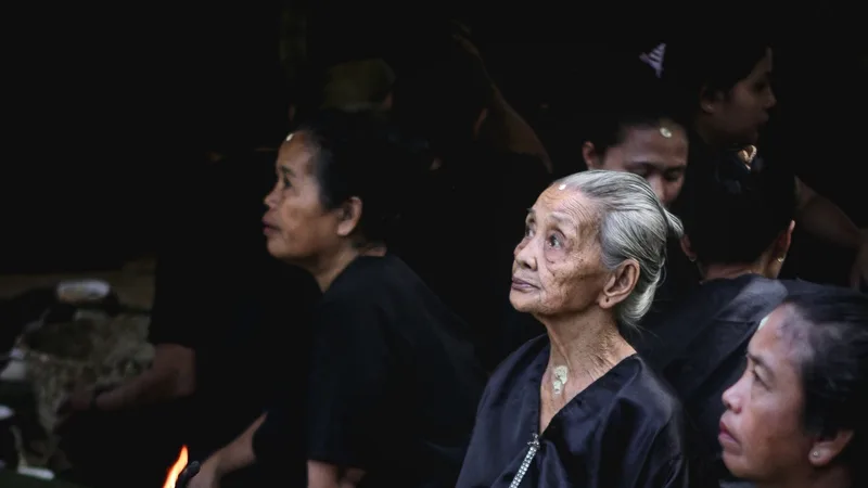 Apa Itu Ammatoa Kajang? Kawasan Adat di Bulukumba Perempuan lanjut usia berambut putih dan berbaju hitam duduk menengadah di antara warga lain yang juga berpakaian hitam dalam ritual Andingingi, dengan nyala api kecil di bawah