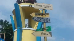 Papan penunjuk bertuliskan Stadion Kanjuruhan Arema Malang di depan tugu berwarna biru kuning