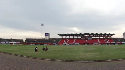 Lapangan dan tribun merah Stadion Kapten I Wayan Dipta di bawah langit mendung