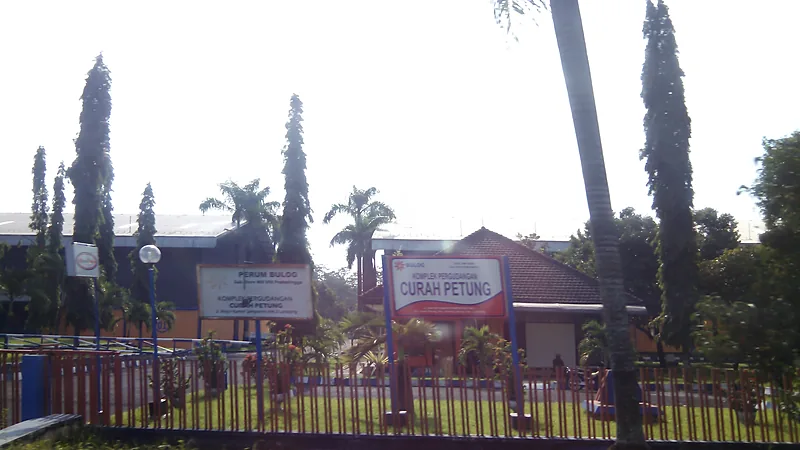 Bantuan Beras Juli-September Disalurkan di Bulukumba Papan nama Komplek Pergudangan Curah Petung milik Perum Bulog di depan bangunan gudang beratap merah, dibatasi pagar besi