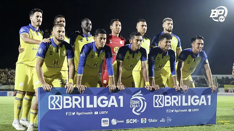 Pemain Barito Putera berkostum kuning biru berfoto bersama pada laga malam di belakang papan BRI Liga 1