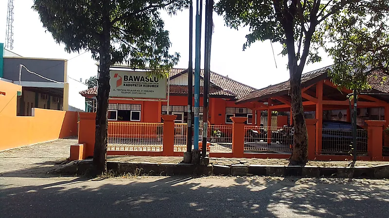 Bawaslu Bulukumba Koordinasi dengan Polres dan Lapas Kantor Bawaslu kabupaten berdinding oranye dan beratap genteng, dengan papan nama di halaman dan pagar besi oranye, dinaungi pepohonan di tepi jalan