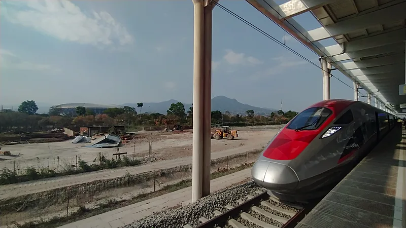Kereta cepat berwarna merah dan perak di peron stasiun dengan Stadion Gelora Bandung Lautan Api terlihat di kejauhan di bawah langit biru