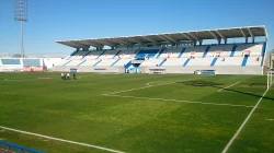 Tribun utama Stadion Butarque berkursi putih dan biru di bawah atap panjang, dilihat dari sudut lapangan pada siang hari