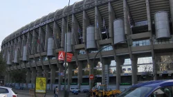Bagian depan Estadio Santiago Bernabéu dengan menara silinder, bendera, dan jalan di depannya