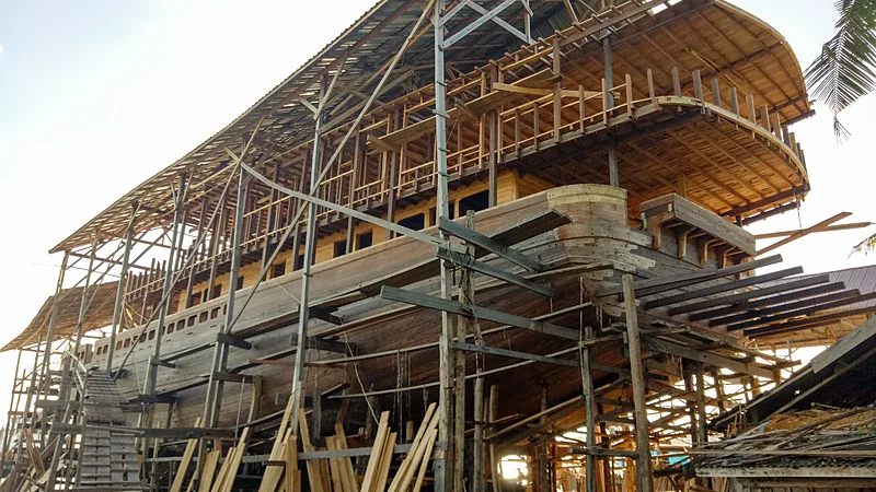 Lambung kapal pinisi kayu setengah jadi berdiri di atas perancah bambu di galangan terbuka