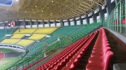 Tribun Stadion Patriot Candrabhaga dengan barisan kursi merah, kuning, dan hijau di bawah atap rangka baja kuning