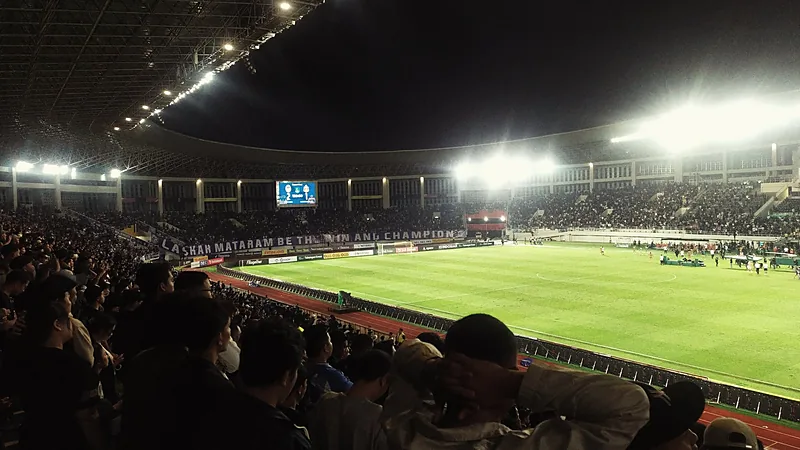Madura United Comeback Tekuk PSIM 2-1, Naik ke Puncak Suporter PSIM memadati tribun stadion pada malam hari dengan lampu sorot menyala dan spanduk bertuliskan Laskar Mataram di seberang lapangan