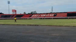Tribune merah hitam bertuliskan BALI UNITED di Stadion Kapten I Wayan Dipta dengan lapangan dan beberapa pemain di kejauhan