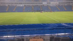 Lapangan hijau stadion dengan tribun biru yang lengang saat para pemain Persiba Balikpapan dan Kendal Tornado FC berkumpul di tengah lapangan