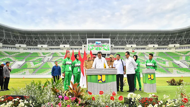 Rombongan pejabat berdiri di tepi lapangan Stadion Utama Sumatera Utara saat peresmian, dengan tribun berkursi hijau putih dan papan skor besar di latar belakang