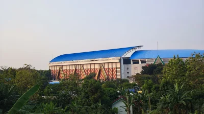 Bangunan Stadion Jatidiri Semarang beratap biru dengan ornamen merah di balik pepohonan