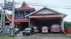 Markas pemadam kebakaran bercat merah putih dengan tiga mobil damkar terparkir di garasi terbuka