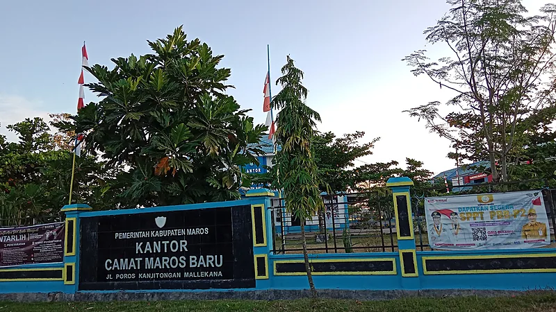Kekeringan Maros Meluas, 200 Ribu Warga Terdampak Gerbang dan pagar biru muda Kantor Camat Maros Baru dengan papan nama hitam bertuliskan Pemerintah Kabupaten Maros, dua bendera merah putih, pepohonan, dan spanduk layanan pajak di sisi kanan