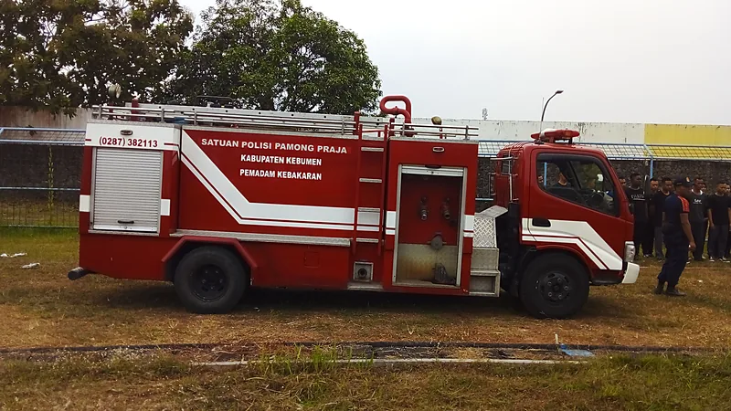 Mobil pemadam kebakaran merah bertuliskan Satuan Polisi Pamong Praja Kabupaten Kebumen Pemadam Kebakaran terparkir di lapangan berumput kering
