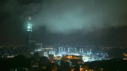 Menara jam Abraj Al Bait menyala hijau di tengah kabut malam dengan kompleks Masjidil Haram terang di kejauhan
