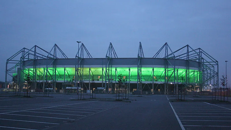 Borussia-Park Mönchengladbach pada senja hari dengan lampu hijau menyala di bawah rangka atap baja