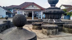 Monumen PSSI di Yogyakarta dengan patung bola batu di atas tumpuan bertingkat dan bangunan beratap genting bertuliskan Monumen PSSI di belakangnya