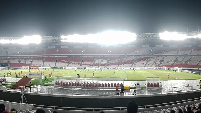 Lapangan Stadion Utama Gelora Bung Karno pada malam hari dengan lampu sorot menyala dan tribun merah putih yang sebagian kosong