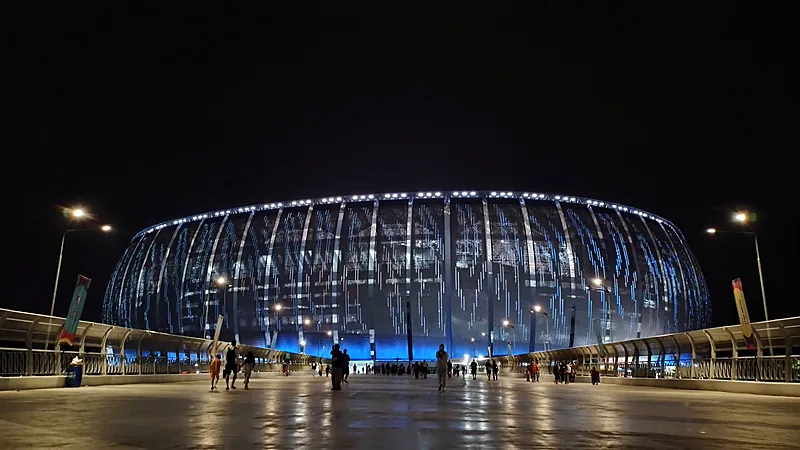 Jakarta International Stadium bermandikan lampu biru pada malam hari dilihat dari jembatan pejalan kaki