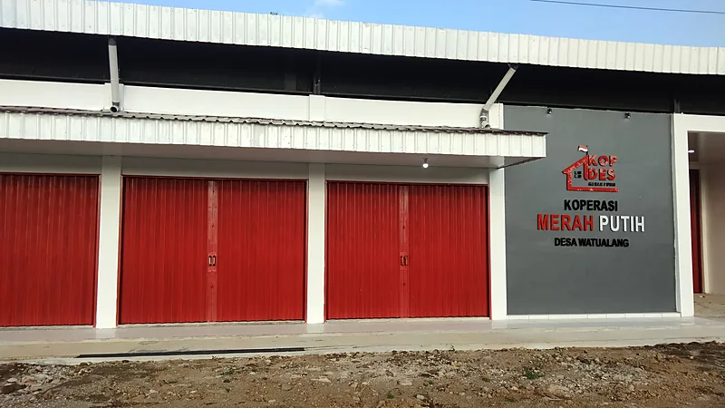 Deretan rolling door merah pada bangunan koperasi dengan papan bertuliskan Koperasi Merah Putih Desa Watualang