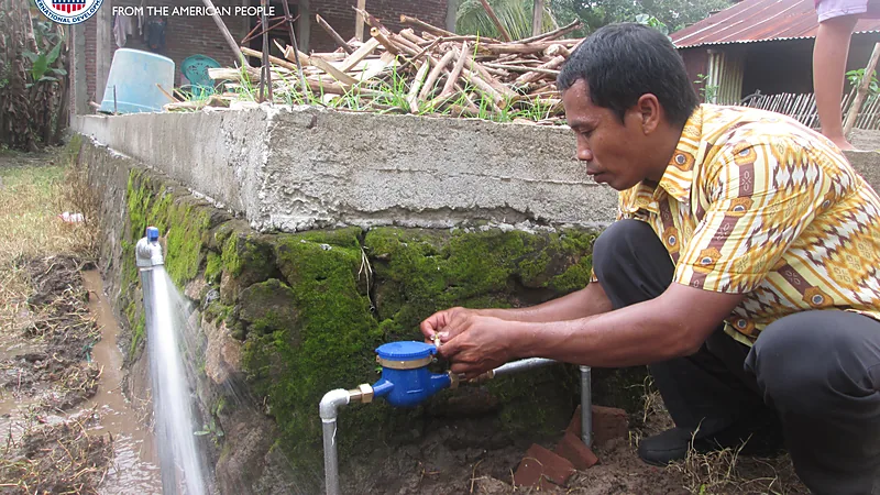 Damkar Bulukumba Salurkan 18 Ribu Liter Air ke Tiga Titik Seorang pria berjongkok memeriksa meteran air biru pada sambungan pipa di halaman rumah