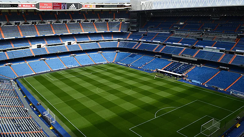 Interior Santiago Bernabéu dengan lapangan hijau bergaris dan tribun biru bertingkat yang masih kosong