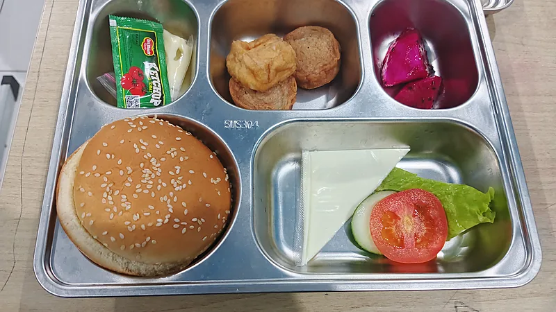 Nampan stainless berisi roti burger wijen, tahu goreng, potongan buah naga, saus, tomat, dan selada