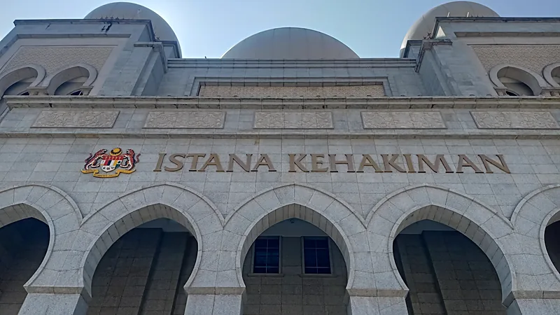 Fasad batu gedung Istana Kehakiman Putrajaya bertuliskan ISTANA KEHAKIMAN dengan lambang Malaysia, deretan lengkungan, dan tiga kubah di atapnya