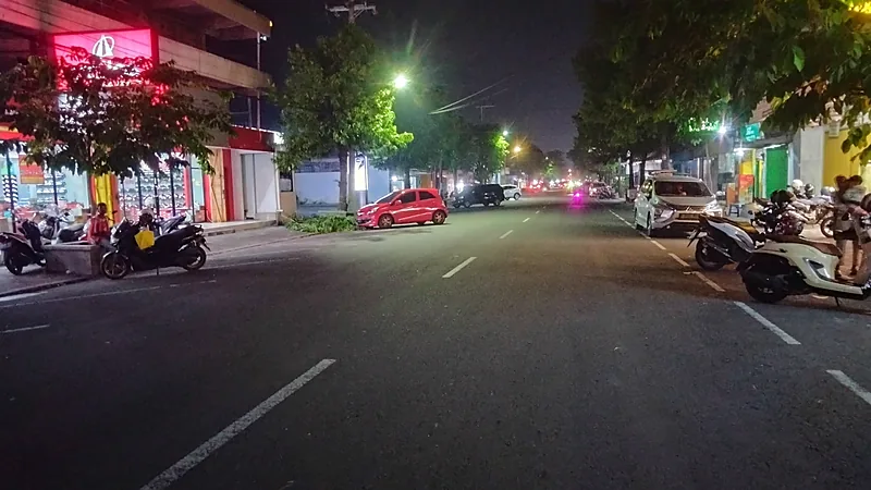 Polres Bulukumba Patroli Malam di Bintarore dan Kalumeme Ruas jalan kota yang lengang pada malam hari, diterangi lampu jalan dan papan nama toko, dengan sepeda motor terparkir di kedua sisi bahu jalan
