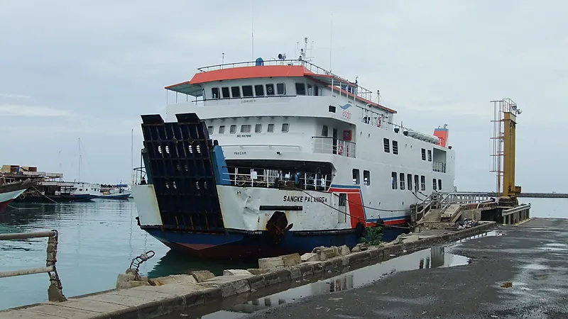 Kapal feri putih bergaris biru dan merah bertuliskan Sangke Palangga bersandar di dermaga beton dengan pintu rampa buritan terbuka
