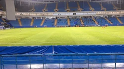 Pertandingan malam di Stadion Batakan dengan tribun biru bertingkat dan pemain di lapangan