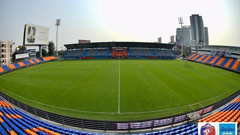 Persib Libur Saat Jeda, Tolic Hadapi 10 Laga dalam 32 Hari Lapangan hijau PAT Stadium di Bangkok dikelilingi kursi tribun biru dan oranye dengan gedung tinggi di kejauhan