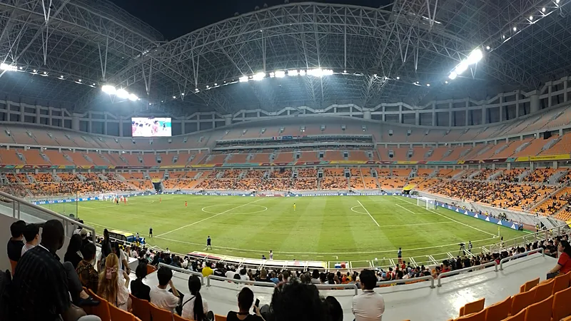 Persija Ajukan Banding atas Sanksi Usiran Komdis PSSI Interior Jakarta International Stadium dengan tribun oranye bertingkat dan atap rangka baja saat pertandingan malam