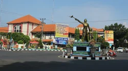 Tugu Kartini di bundaran jalan Kota Jepara dengan gedung beratap genting dan papan reklame di latar belakang