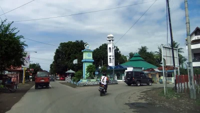 Ruas jalan di Kabupaten Bulukumba dengan tugu, menara masjid putih, dan masjid beratap hijau