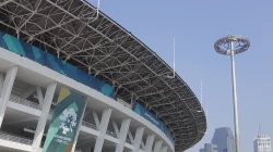 Fasad melengkung Stadion Utama Gelora Bung Karno dengan rangka atap baja dan tiang lampu di bawah langit biru