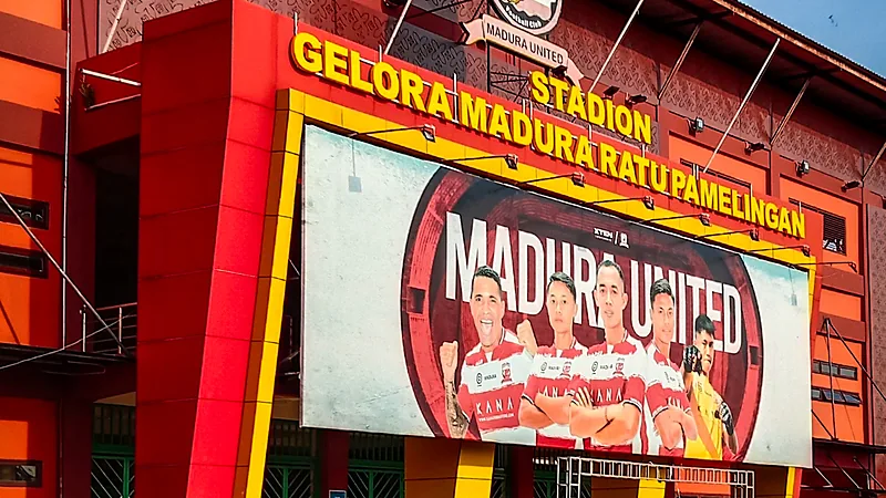 Papan nama Stadion Gelora Madura Ratu Pamelingan dan baliho Madura United di fasad stadion berwarna oranye