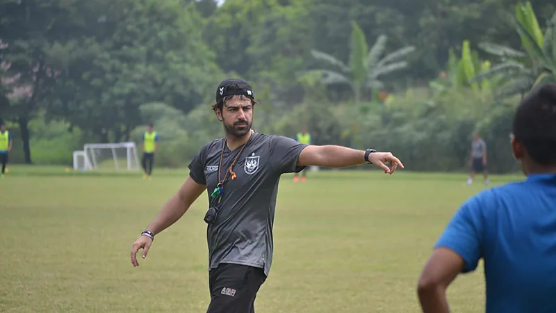 Seorang pelatih berkaus abu-abu berlogo PSIS memberi instruksi sambil menunjuk ke arah lapangan pada sesi latihan di lapangan rumput