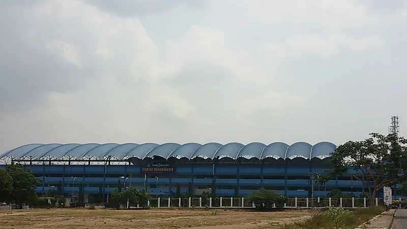 Bangunan luar Stadion Maguwoharjo, Sleman, dengan deretan atap melengkung berwarna biru pada siang hari