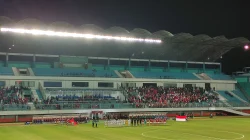 Barisan pemain dan ofisial berjajar di tengah lapangan Stadion Maguwoharjo pada laga malam, dengan tribun yang sebagian terisi penonton