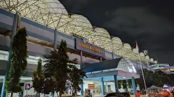 Pintu masuk utama Stadion Maguwoharjo pada malam hari dengan papan nama stadion dan atap rangka baja yang diterangi lampu