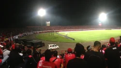 Suporter berkaus merah menonton pertandingan malam di Stadion Kapten I Wayan Dipta, dengan lampu sorot menyala di atas tribun yang penuh