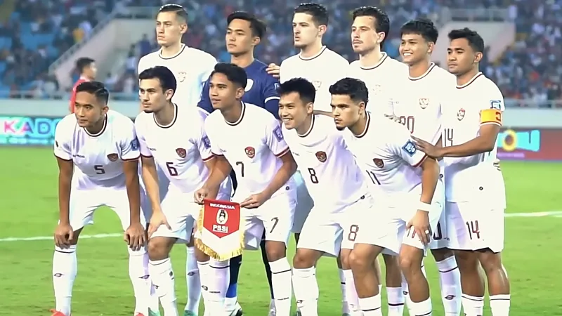 Sebelas pemain Timnas Indonesia berseragam putih berfoto bersama sebelum pertandingan, salah satunya memegang panji PSSI