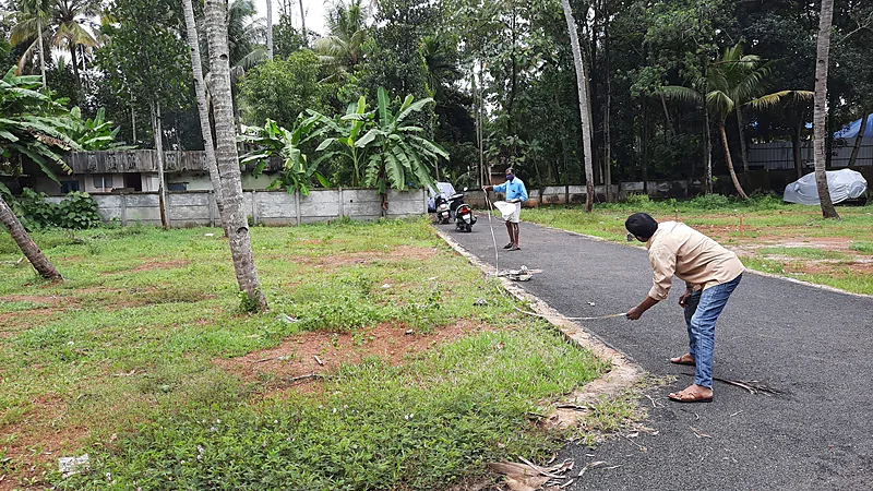 BPN Usul Ukur Ulang Lahan Bontomanai yang Disengketakan Dua orang membentangkan meteran gulung menyusuri tepi jalan beraspal di sebidang tanah kosong berumput yang dikelilingi pohon kelapa