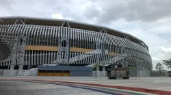 Sisi luar Stadion Nasional Bukit Jalil dengan fasad bersirip abu-abu dan aksen kuning di bawah langit berawan