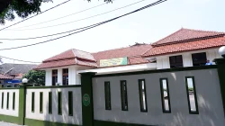 Gedung pengadilan beratap genteng merah di balik pagar tembok putih berlis hijau, dengan lambang pengadilan terpasang pada pagar