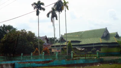 Kompleks bangunan sekolah beratap genteng hijau dengan pagar tembok pirus dan deretan pohon pinang