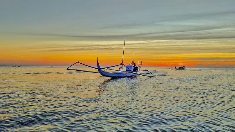 Solar Subsidi Sulsel Diproyeksi Lampaui Kuota 10,4 Persen Perahu kayu bercadik dengan satu orang di atasnya melaju di laut tenang berwarna keperakan saat langit jingga menjelang matahari terbit, dengan perahu lain di kejauhan